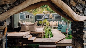 Un espace extérieur rustique doté d’une terrasse en bois, de meubles en osier et de camping-cars d’époque.