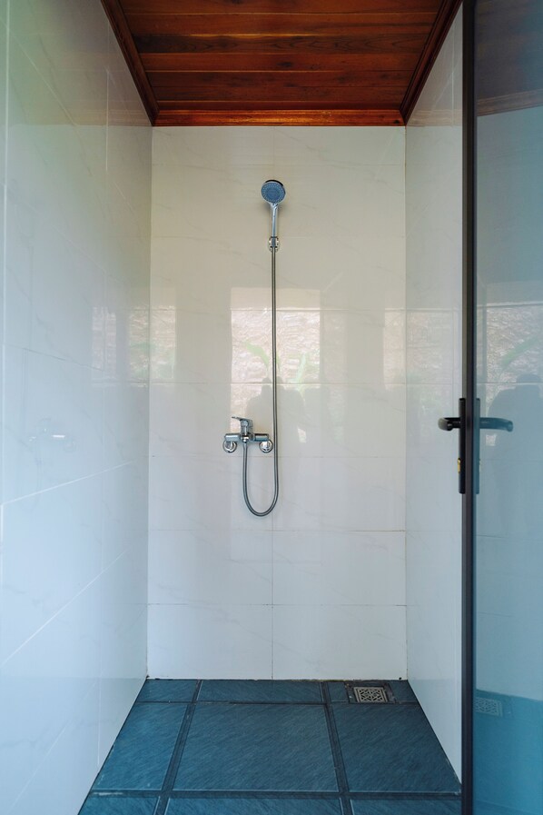 Une douche équipée d’un pommeau de douche à main et d’un robinet mural, ainsi qu’un sol carrelé et un plafond en bois.
