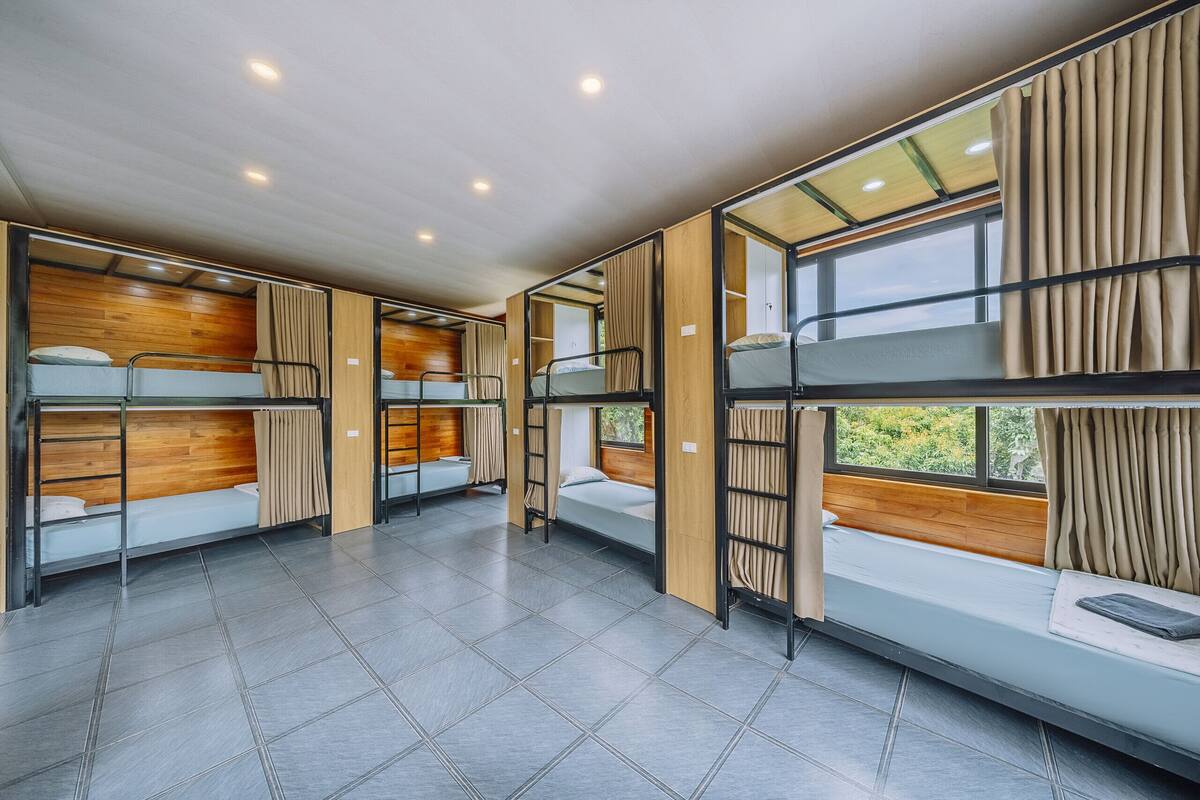Un dormitorio con literas, paredes de paneles de madera y ventanas grandes con cortinas.