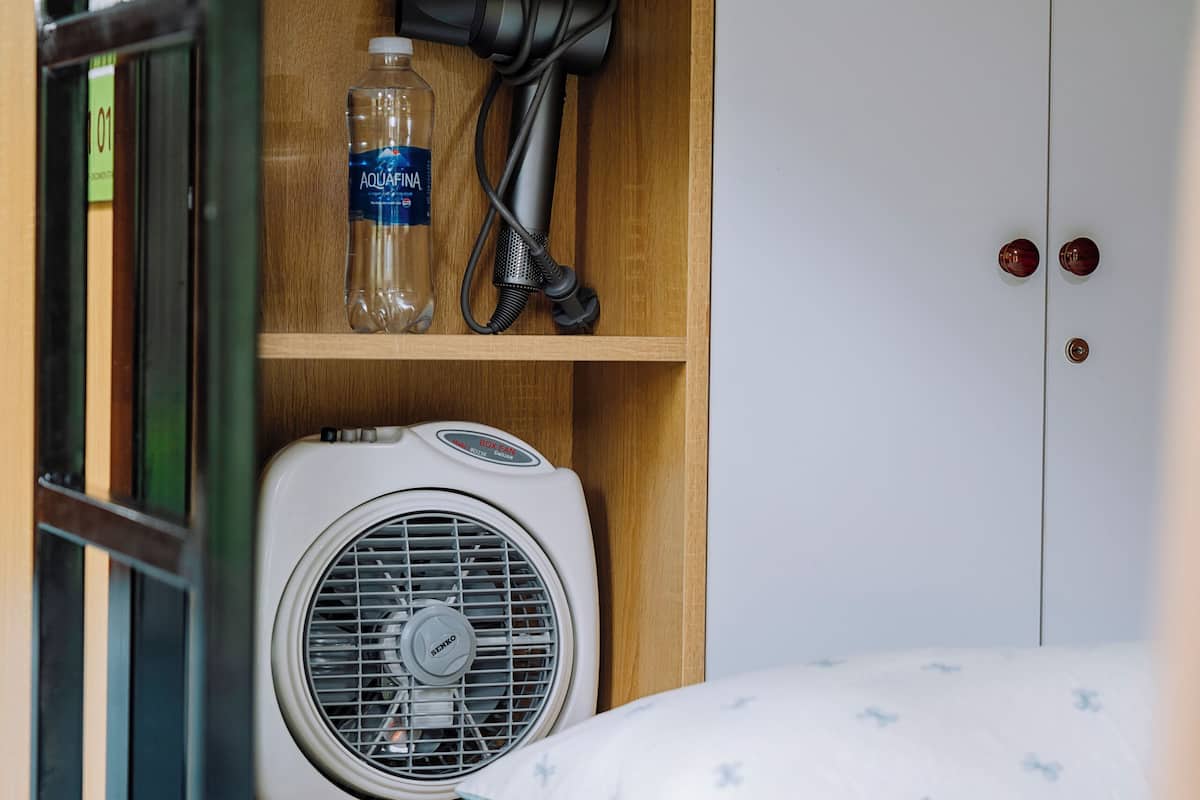 Una cama litera con un ventilador, una botella de Aquafina y un secador de pelo sobre una estantería.