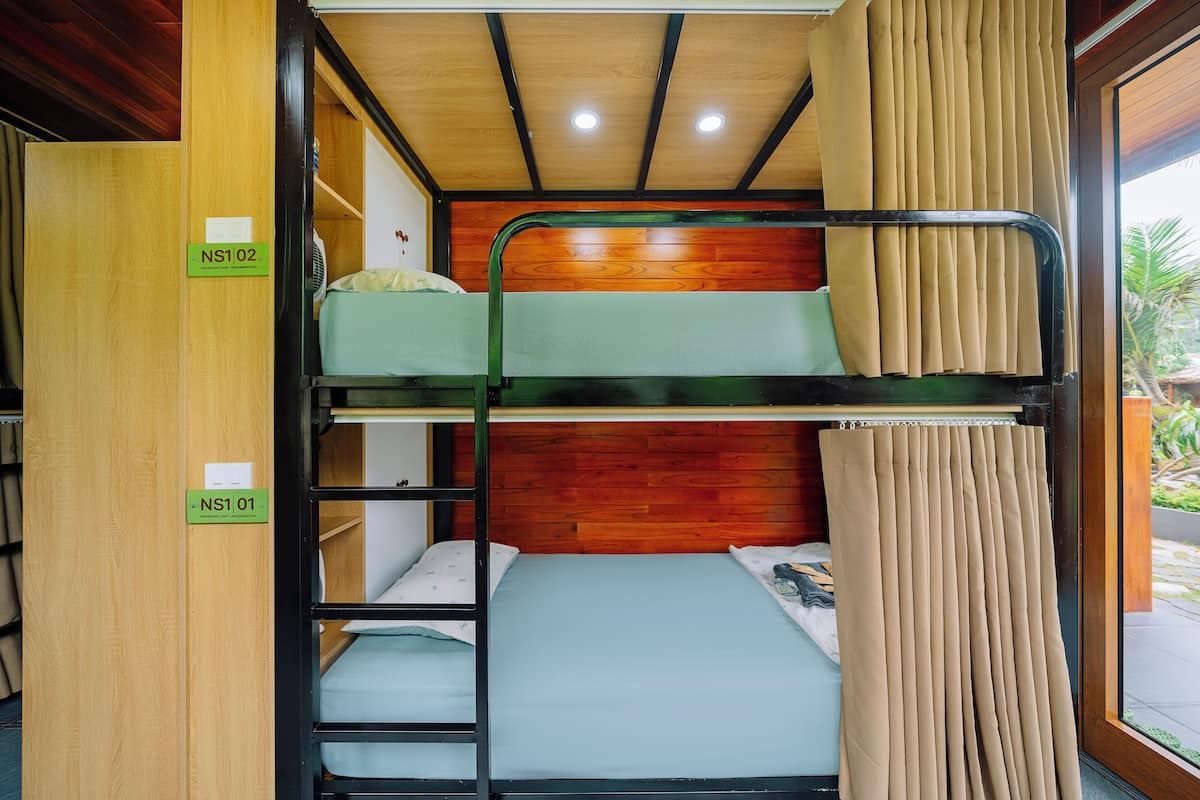 Dormitorio con literas, paneles de madera y ventana con cortinas.