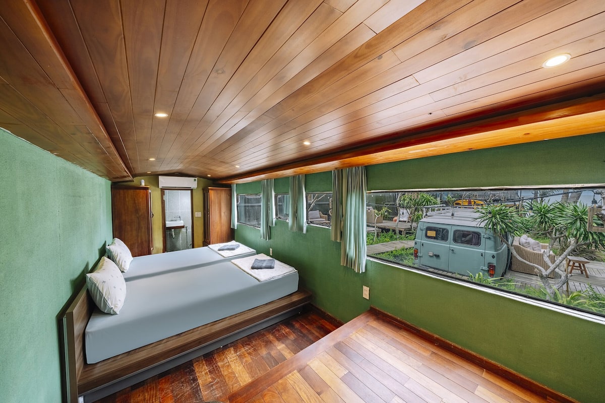 Una habitación con una cama, una ventana con vista a una camioneta y una pared verde.