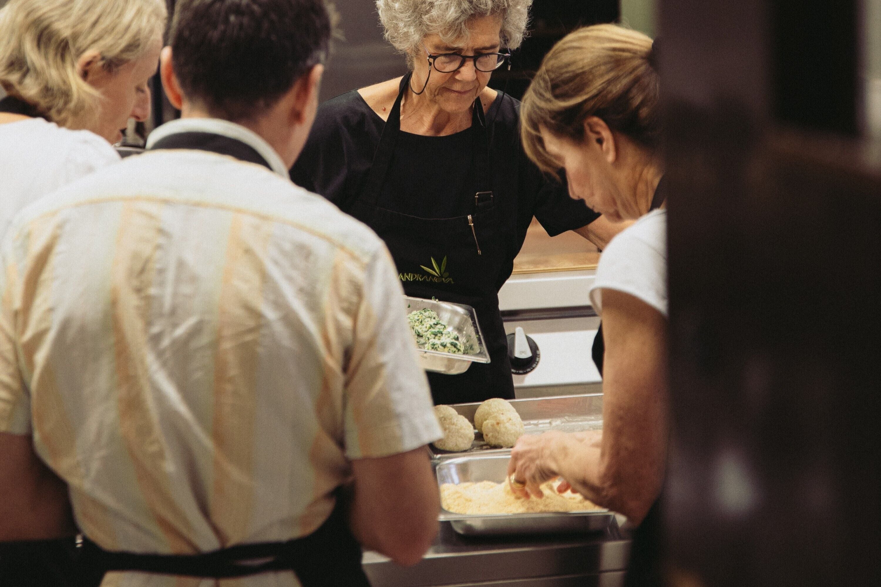 Un groupe de personnes est occupé à préparer des aliments. On voit un plateau rempli de différents plats et une personne portant un tablier noir.