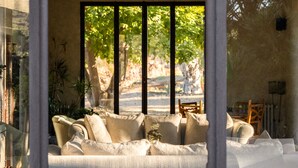 A room with a sofa, a chair, and a window with a view of trees and a path. - Mandranova Farm (Palma di Montechiaro)