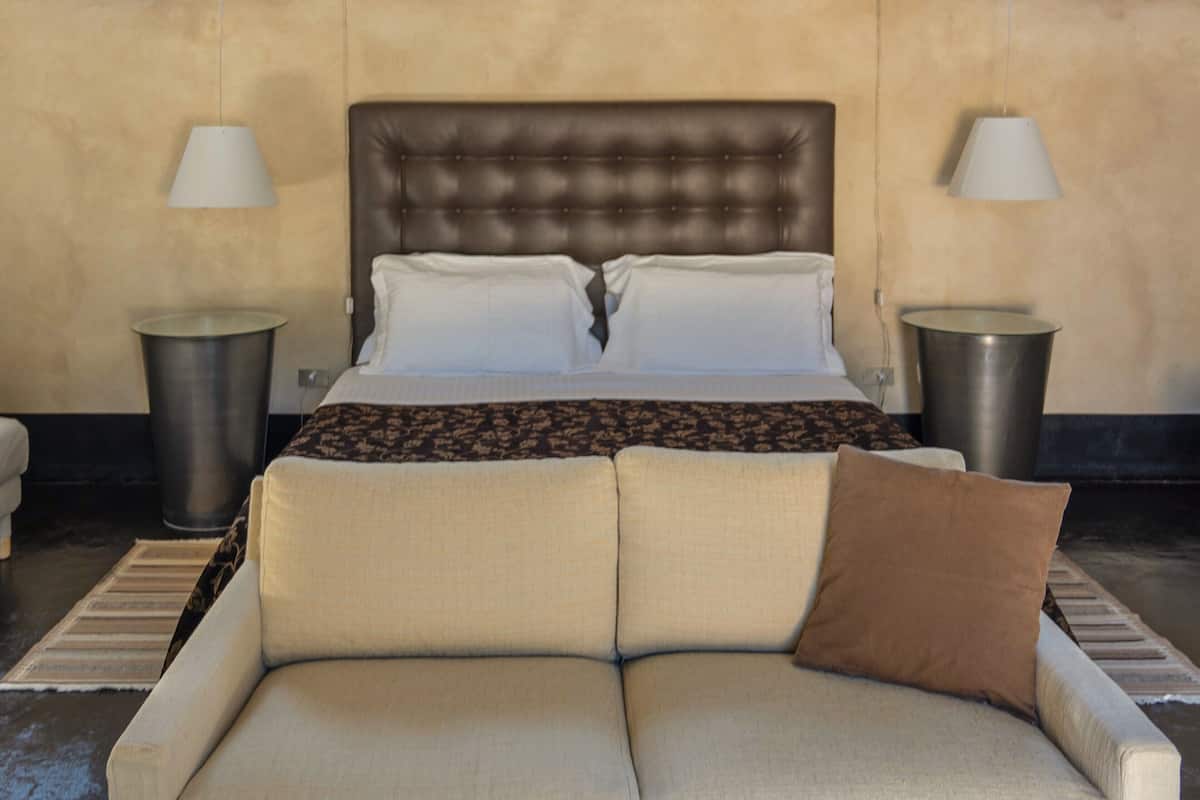 Ein Schlafzimmer mit einem Bett, zwei Nachttischlampen, einem Sofa und einer gemusterten Decke.