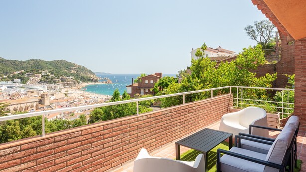Un balcon donnant sur une ville côtière, un mur de briques et du mobilier d’extérieur.