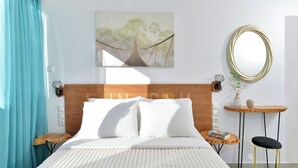 A neatly arranged bedroom with a bed, bedside tables, a small round table, a chair, a wall-mounted mirror, and a framed picture. - SunDay Free Airport Shuttle (Spata-Artemida)