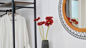 A white shirt hanging on a rack, a vase with red flowers, and a mirror with a geometric frame. - SunDay Free Airport Shuttle (Spata-Artemida)