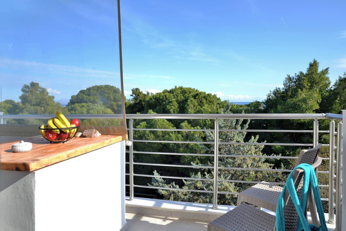 Ein Balkon mit Holztisch, Obstschale, Metallgeländer und Korbstühlen.