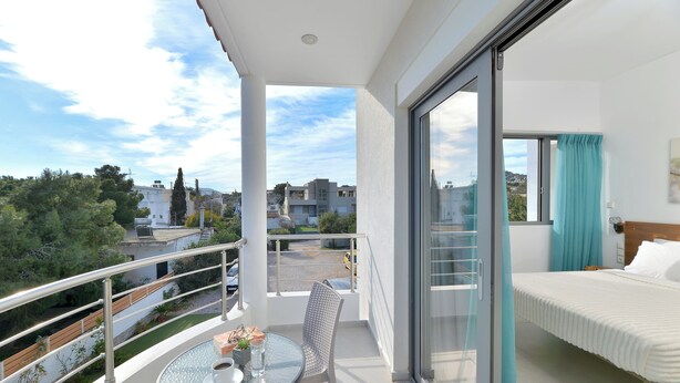 A balcony with a table, chair, and a bed with a view of the city. - SunDay Free Airport Shuttle (Spata-Artemida)