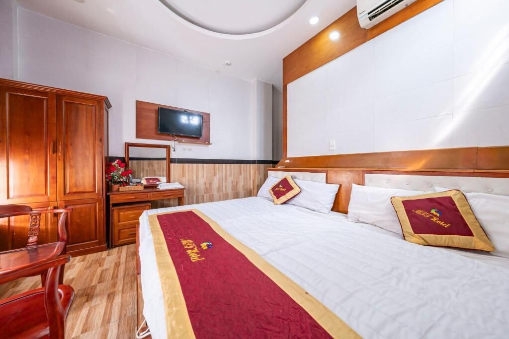 A hotel room with a large bed, wooden furniture, a flat-screen TV, and a red bed runner.
