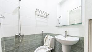 A bathroom with a toilet, a sink, a shower, and a mirror. - Hotel Airport MTT (Ho Chi Minh City)