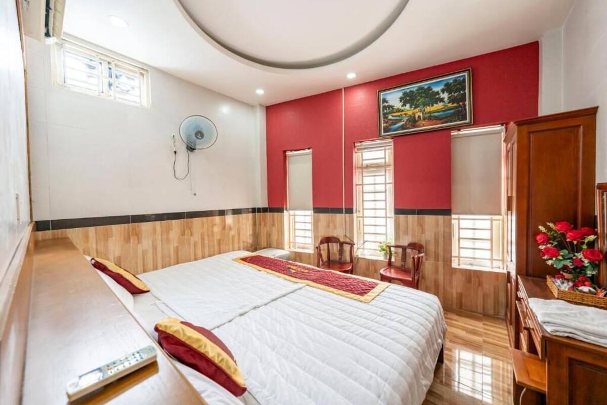 A hotel room with a large bed, a desk, a chair, a fan, and a painting on the wall.