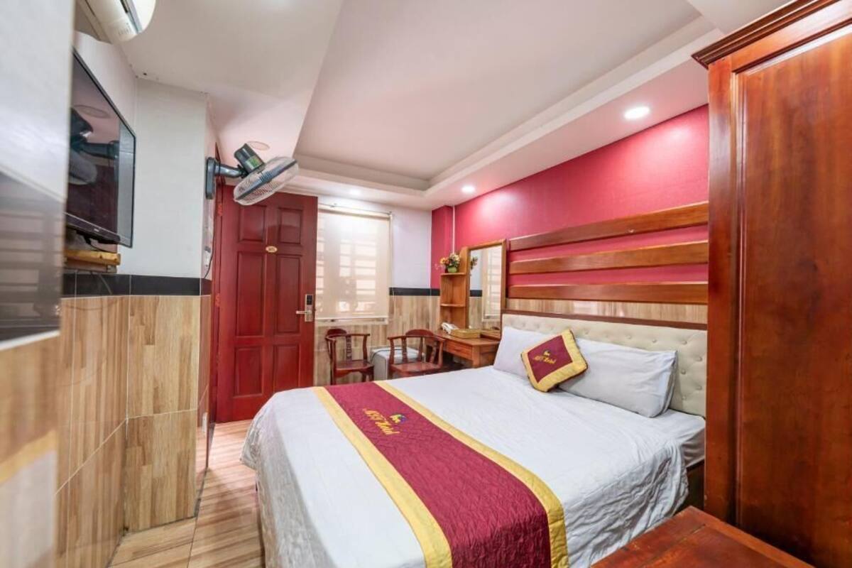 A hotel room with a bed, a desk, a chair, a TV, and a red door.