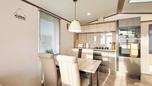 Una cocina moderna con electrodomésticos de acero inoxidable, un comedor con mesa y sillas, y un cartel que indica prohibido fumar y vapear.