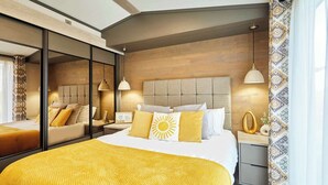 Habitación de hotel moderna con una cama grande, un espejo, cabecera de madera, lámparas de noche y cortina estampada.