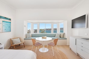 Ein Zimmer mit einem runden Tisch, zwei Korbstühlen, einer Couch mit Blick, einem Fernseher und einem weißen Schrank.