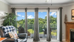 Un salon avec un canapé en cuir, une cheminée et une vue sur un balcon, accessible par une porte-fenêtre coulissante.