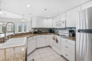 A modern kitchen with white cabinets, stainless steel appliances, granite countertops, and a tiled backsplash. - Golf Vista 171 (Pigeon Forge)