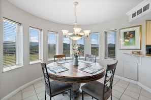 A dining room with a round table, chairs, a chandelier, and large windows with blinds. - Golf Vista 171 (Pigeon Forge)
