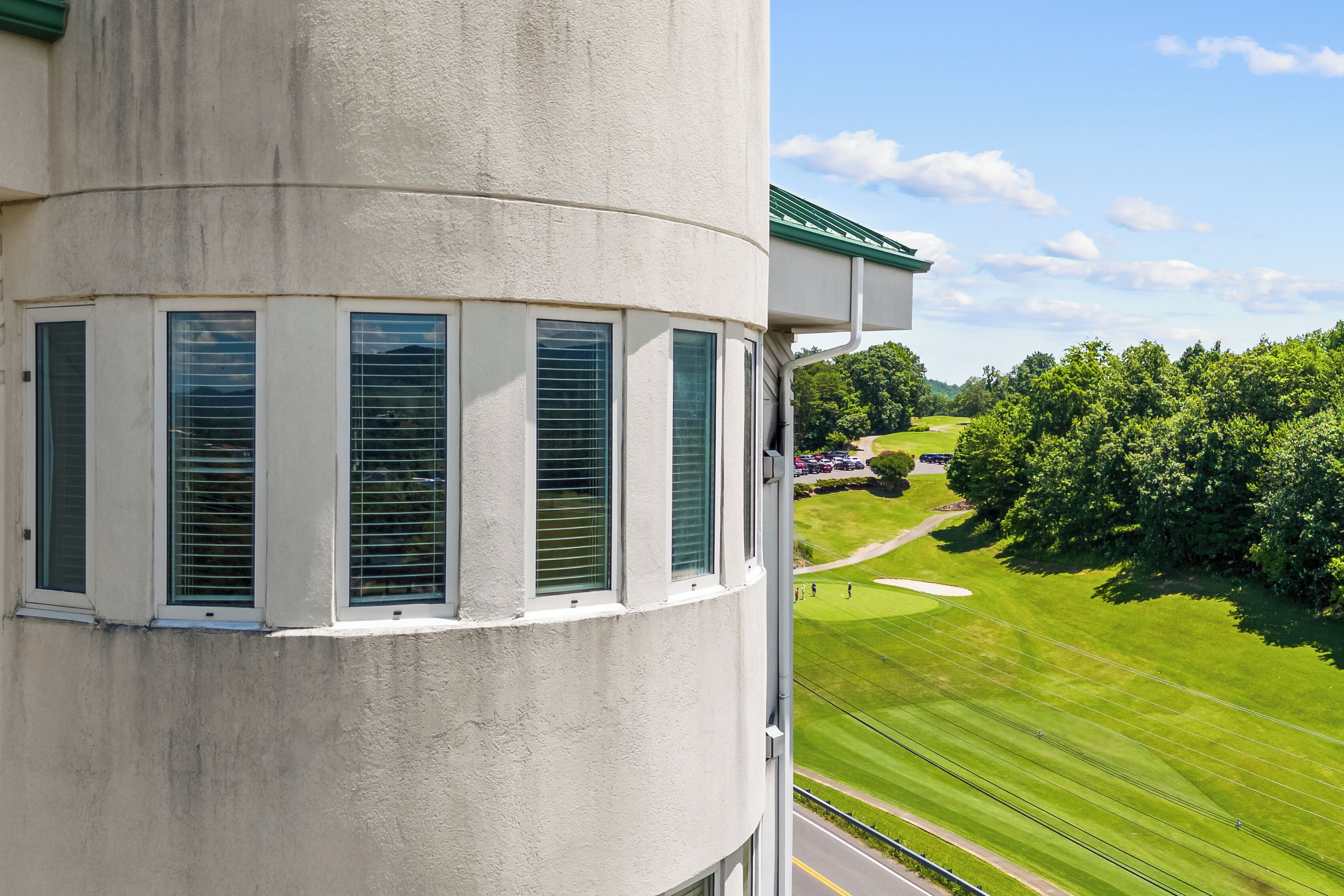 A building with a curved facade, large windows with blinds, and a view of a well-maintained lawn and trees.