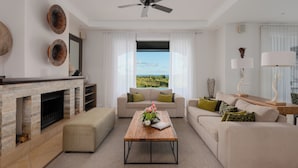 Una sala de estar moderna con chimenea, ventilador de techo, un conjunto de sofás y vistas al exterior.