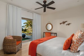 A bedroom with a bed, a wicker chair, a ceiling fan, a large mirror, and a view of the outdoors.