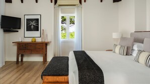 Un dormitorio con cama, mesita de noche, televisor y ventana con cortinas.