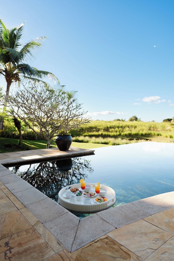 A poolside area with a dining setup, a palm tree, and a view of the landscape.