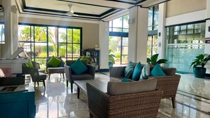 A spacious lobby with a reception desk, seating area with wicker furniture, large windows with a view of greenery, and a glass door leading to the office area. - Luxurious Laguna Phuket Large 2-bedrooms 2 Bathrooms Ensuite With Large Pool (Choeng Thale)