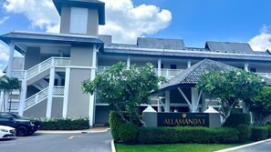 Ein Hotel mit einem Schild, auf dem 'ALLAMANDA 1' steht, einem überdachten Eingang und einer Treppe zu den oberen Etagen.