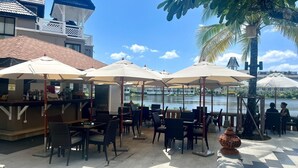 An outdoor dining area with tables and umbrellas, overlooking a body of water. - Luxurious Laguna Phuket Large 2-bedrooms 2 Bathrooms Ensuite With Large Pool (Choeng Thale)