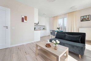 A modern living room with a sofa, a coffee table with flowers, and a kitchen in the background. - Bright Apartment in Lodz | Parking, Balcony, Close to Museum (Łódź)