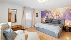 Un dormitorio con cama, mesita de noche, cómoda, silla, espejo y un cuadro en la pared.