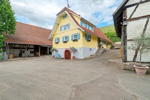 A two-story building with a red-tiled roof, a yellow facade, and a wooden staircase leading to the entrance. - Winzerhof Männle with Garden, Terrace and Wi-Fi (Oberkirch)