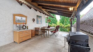 Un patio exterior con mesa y sillas de madera, una parrilla, un armario de madera y un cuadro colgado en la pared.