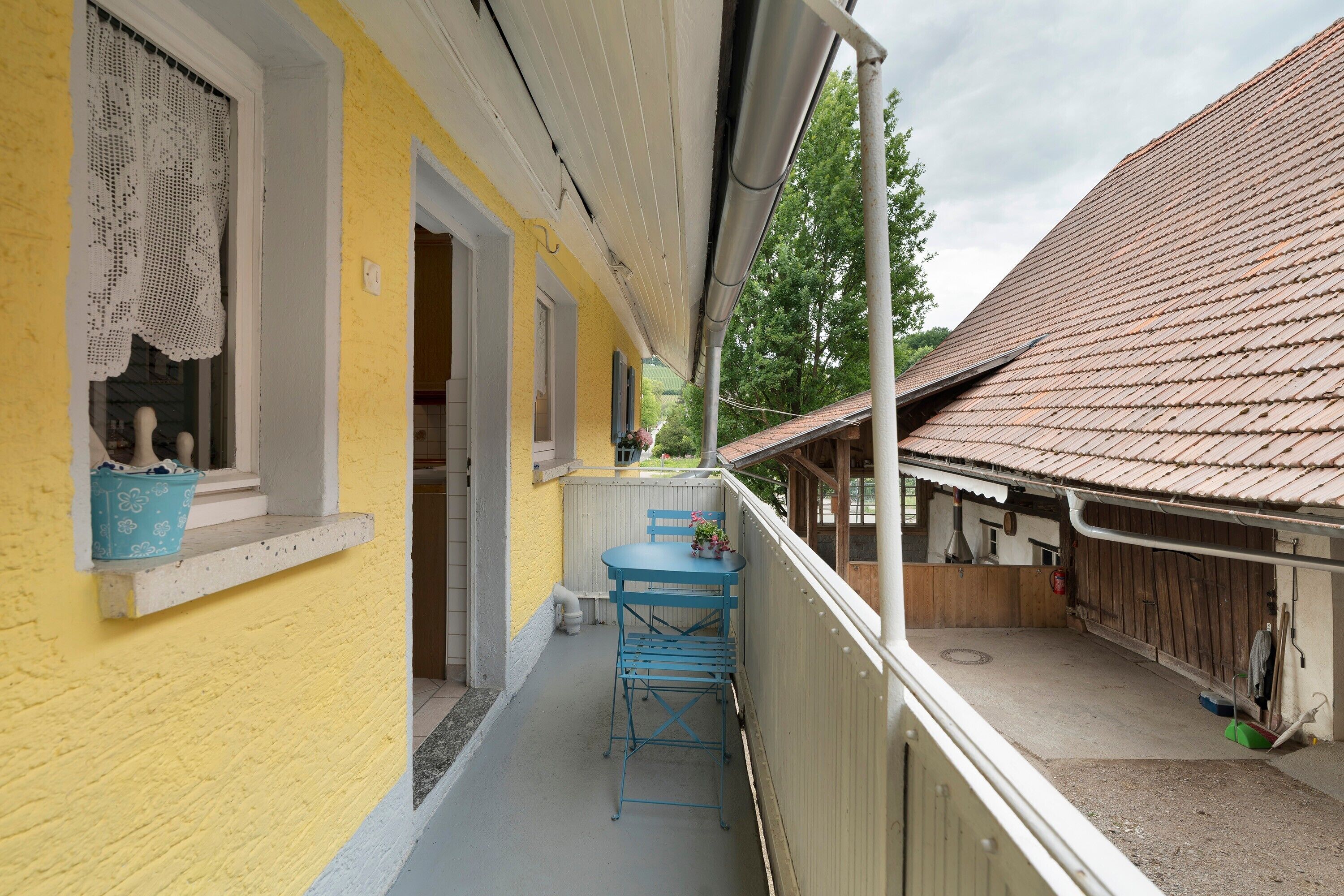 A yellow building with a balcony, a blue table, and a chair.