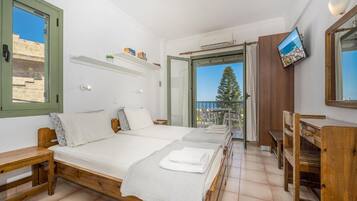 A room with a bed, a desk, a TV, and a balcony with a view of the sea.