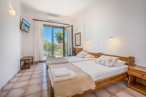 A bedroom with two beds, a wooden nightstand, a small table, and a view of the outdoors. - 123 Soleil (Aegina)