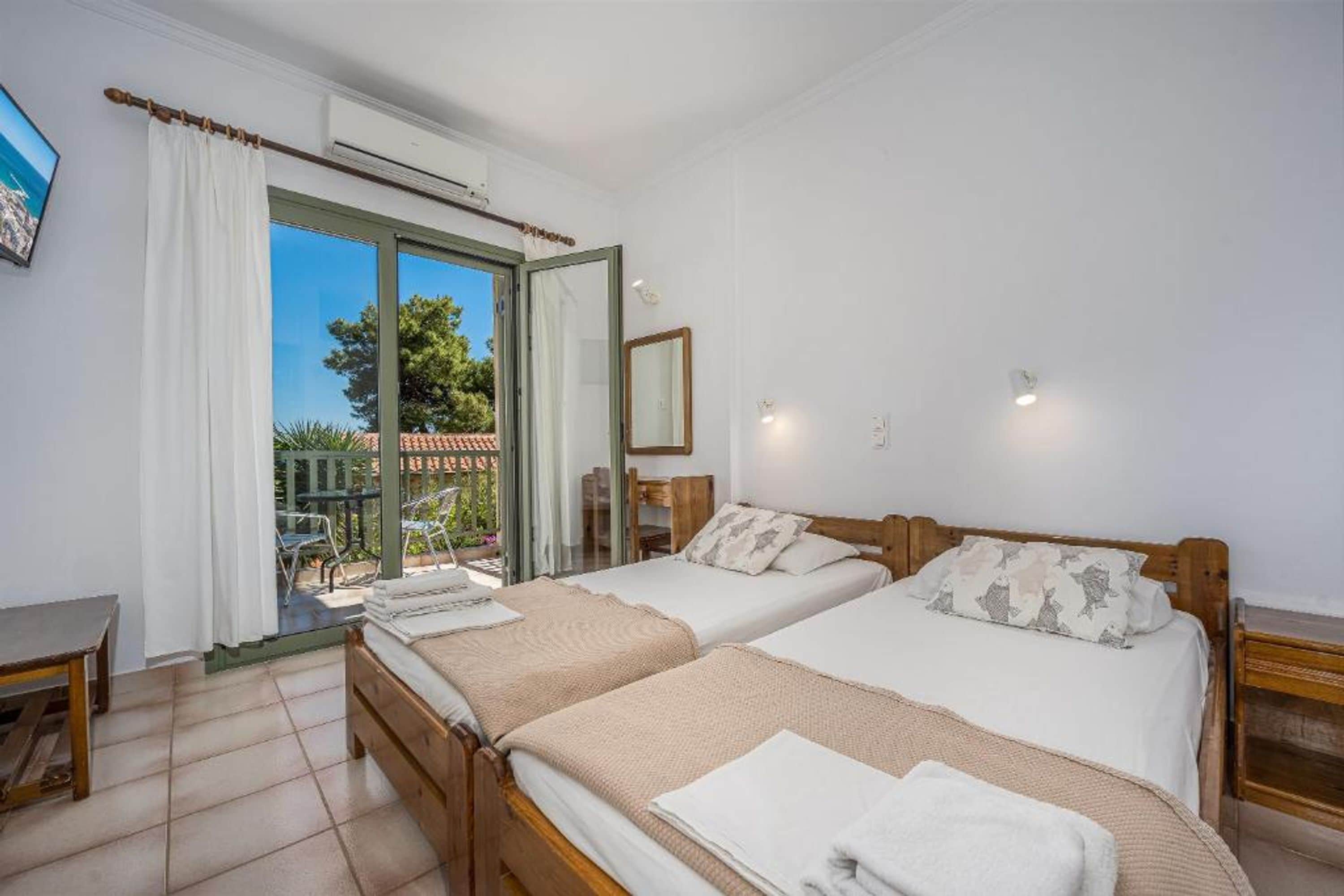 Quarto com duas camas, uma varanda, uma mesa e um espelho.