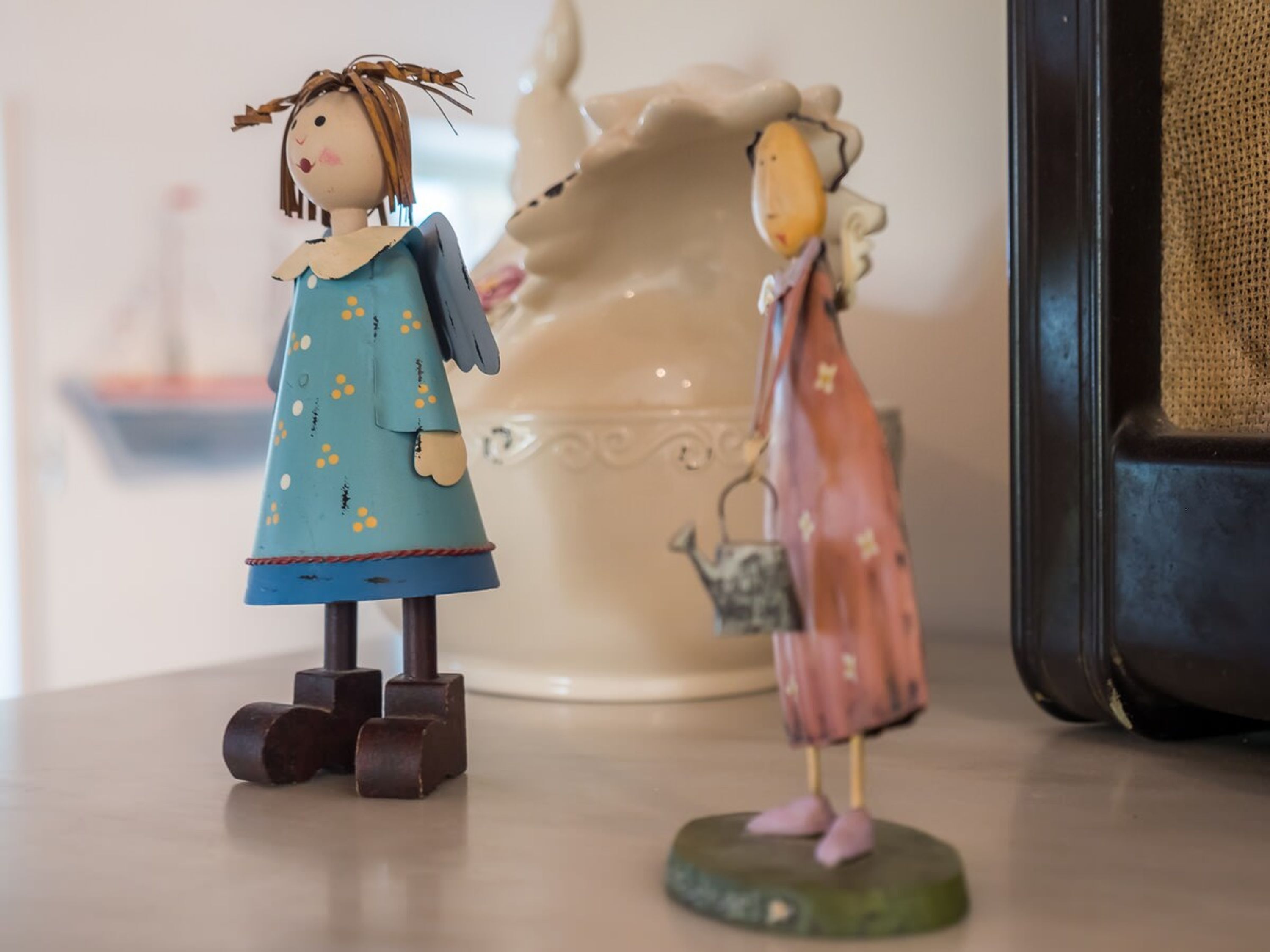 Due figurine su un tavolo, con una vasi di ceramica sullo sfondo.