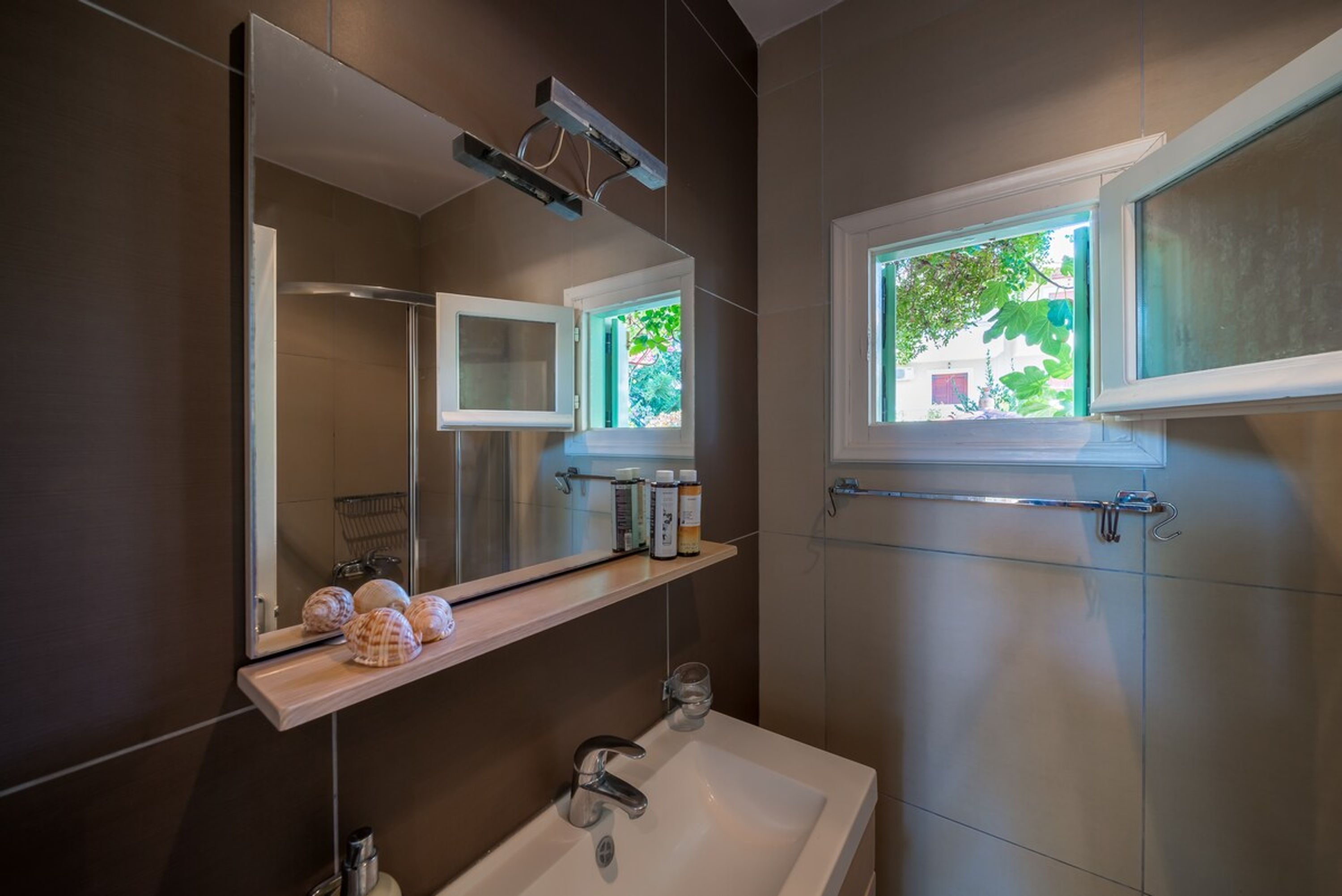 A modern bathroom with a large mirror, a sink, and a window.