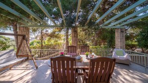An outdoor patio with a wooden table and chairs, a swing, and a covered seating area. - My Little House - 123 Soleil (Aegina)