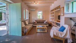 A cozy living room with a sofa, a coffee table, and a bookshelf. - My Little House - 123 Soleil (Aegina)