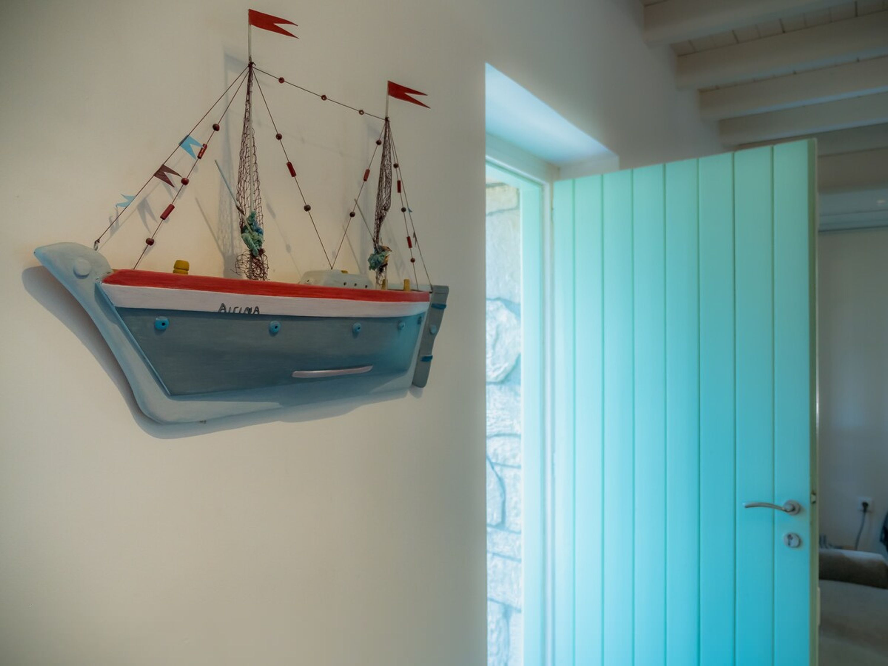 Un modelo de barco en una pared, una puerta color turquesa y una ventana con vistas.
