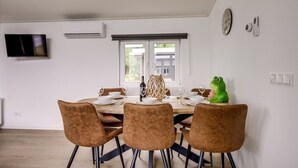 Ein Essbereich mit einem Tisch für vier Personen, einem an der Wand montierten Fernseher und einem Fenster mit Blick auf Grünflächen.