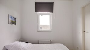 Ein Schlafzimmer mit zwei Betten, einem Fenster mit Jalousie, einem Heizkörper und einer Tür.