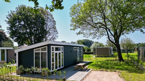 Ein modernes, eingeschossiges Haus mit dunkler Fassade, großen Fenstern und einer Terrassenfläche.