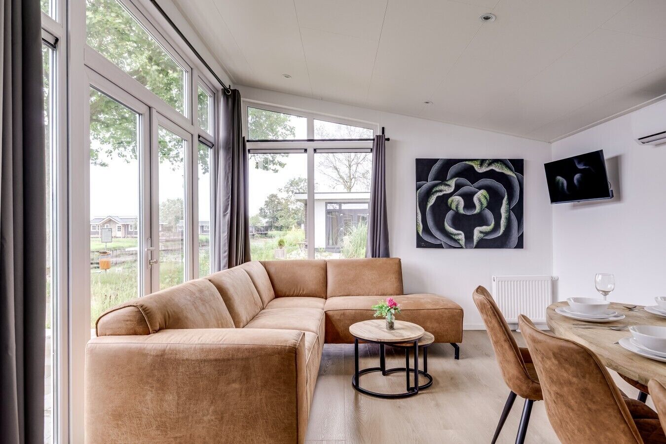 A modern living room with a sectional sofa, a small round table with a vase, and a dining area with a wooden table and chairs.