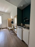 Cozinha compacta com lava-louças, pia e fogão. Há uma área de refeições com uma cadeira e uma mesa.